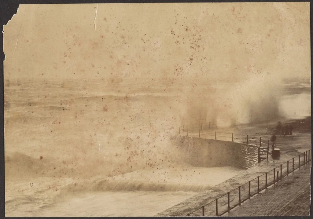 An archival photograph of storm waves breaking over a stone sea wall
