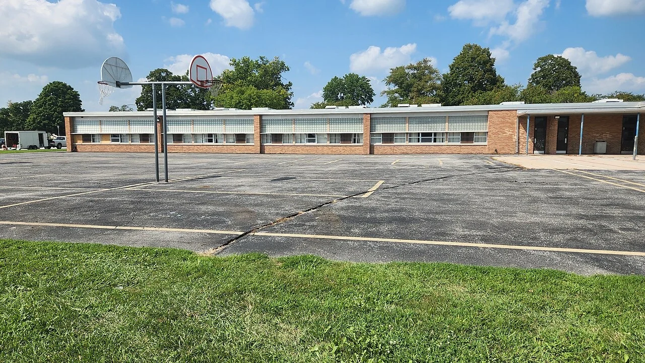 An empty schoolyard with basketball hoops in front of a low brick school